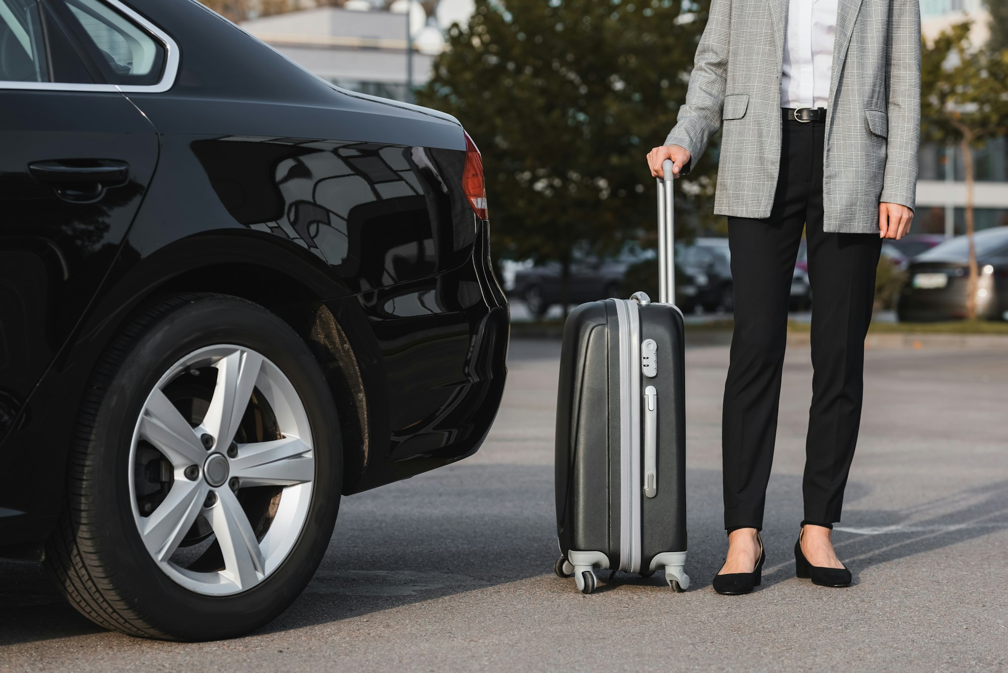 cropped view of businesswoman with suitcase near black car